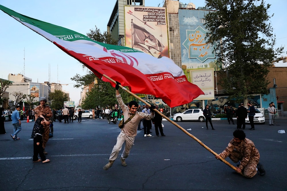 Demonstrators wave a huge Iranian flag in their anti-Israeli gathering in front of an anti-Israeli banner on the wall of a building at the Felestin Sq. in Tehran, Iran, Monday, April 15, 2024. 