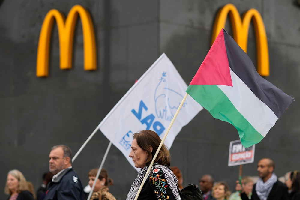Demonstranten mit einer palästinensischen Flagge und einer weiteren mit der Aufschrift „Frieden“ gehen am Samstag, dem 6. April 2024, an einem McDonald's-Restaurant in Lissabon vorbei. (AP)