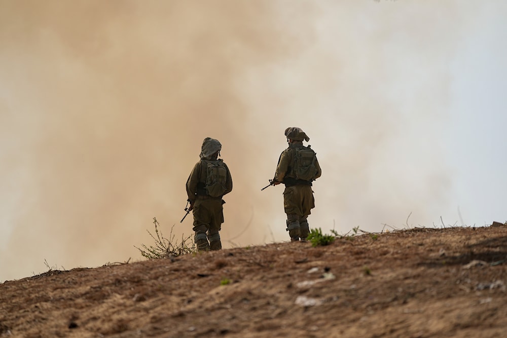 Israeli soldiers stand next to a burning field near the border with the Gaza Strip, on October 24, 2023. (AP)