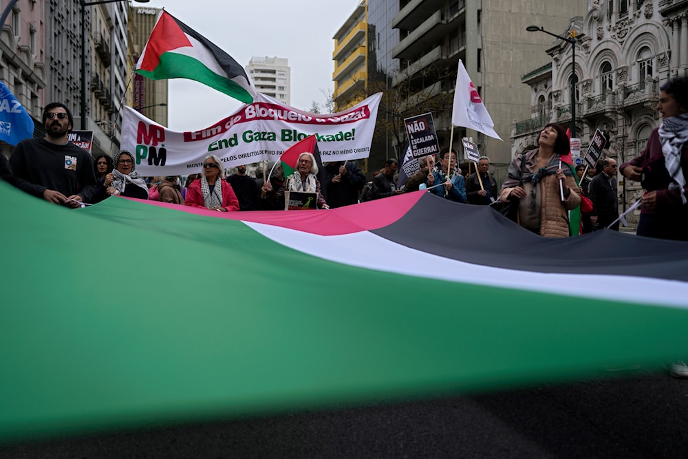 People carry a giant Palestinian flag while marching between the Embassy of 'Israel' and the Portuguese parliament in Lisbon demanding a ceasefire in Gaza and in support of Palestinians, Saturday, April 6, 2024. (AP)