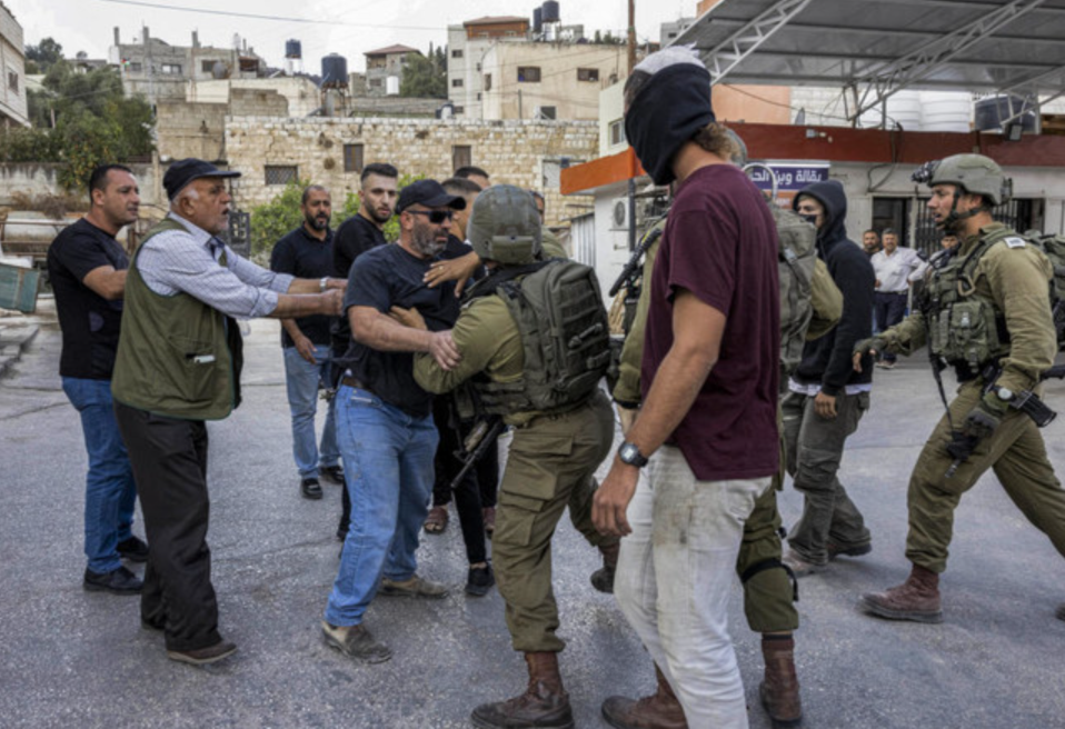 A masked Israeli settler stands by while Palestinians and Israeli soldiers scuffle during clashes in the town of Hawara in the occupied West Bank. 