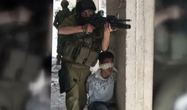 An undated image showing the Israeli occupation forces using a Palestinian child as a human shield. (Social media)
