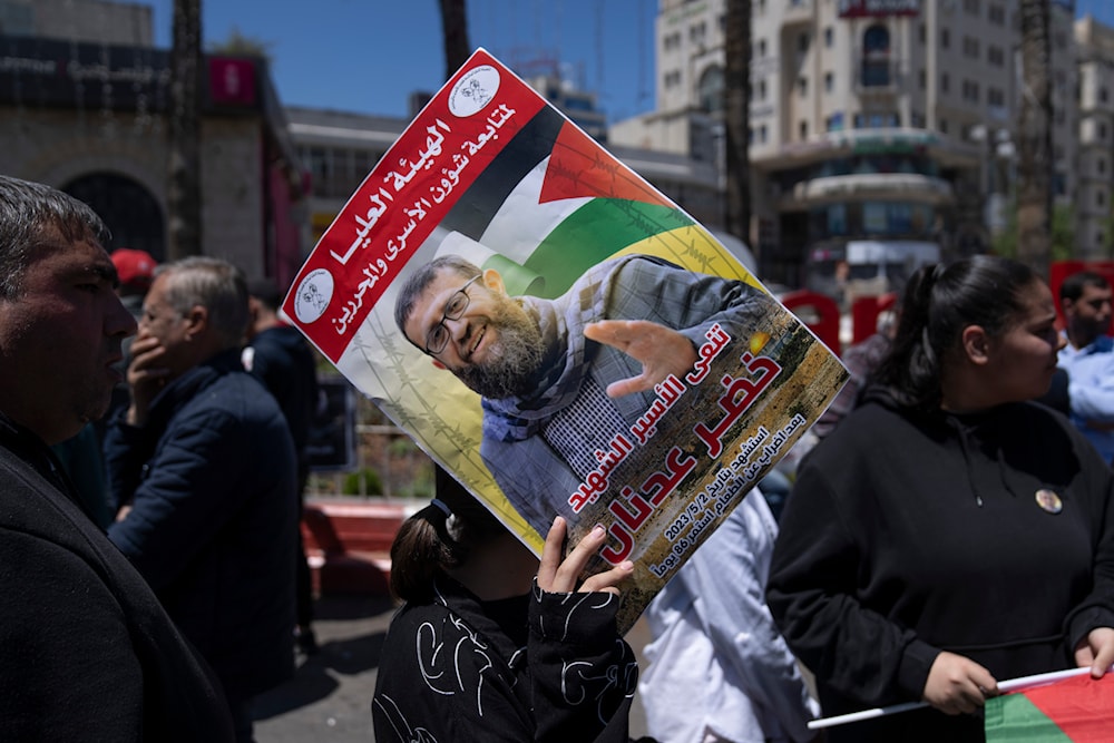 A Palestinian activist holding a poster with the name and picture of PIJ official Khader Adnan, who was martyred after a 86 days hunger strike, during a protest in the West Bank city of Ramallah, May 2, 2023 (AP)