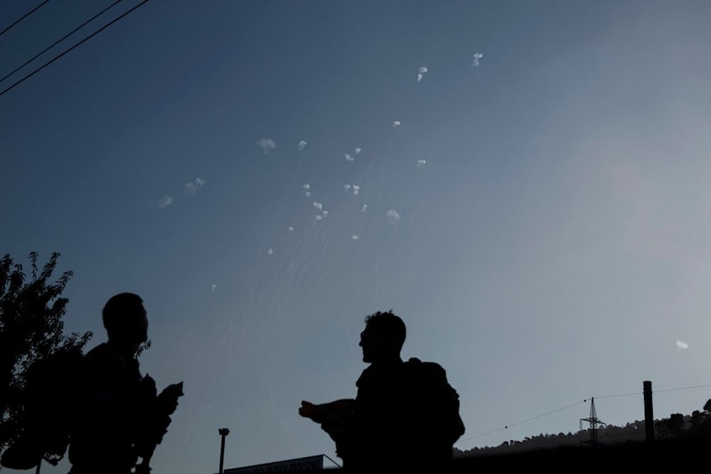 Members of the Israeli forces watch the Iron Dome air defense system firing to intercept rockets launched from Lebanon, in northern occupied Palestine, Wednesday, October 9, 2024 (AP)