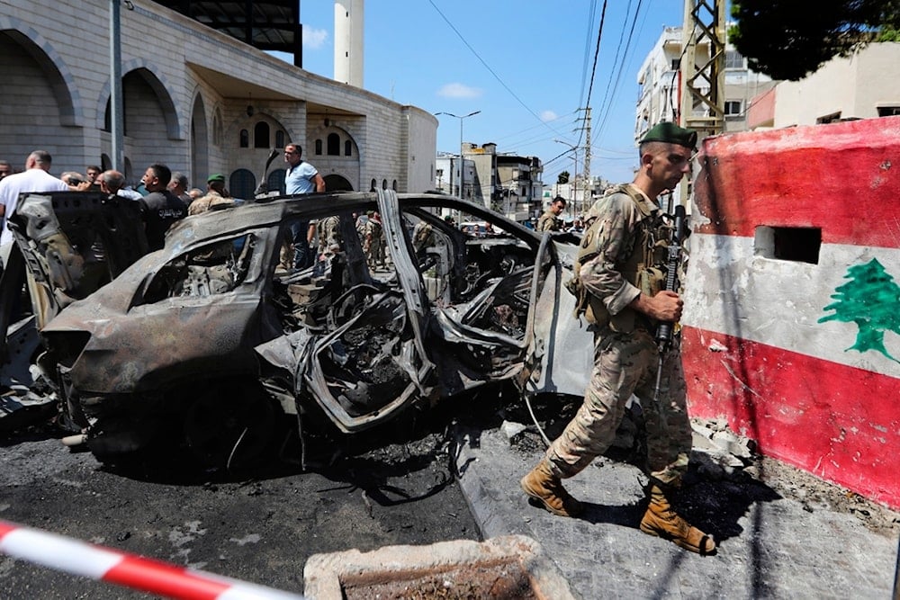 A Lebanese Army soldier passes in front of a car that was hit by an Israeli strike in the southern port city of Sidon, Lebanon, Wednesday, August 21, 2024 (AP)