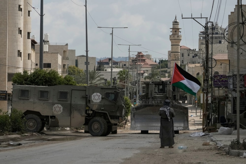  Renowned Palestinian activist Khairi Hanoon waves the Palestinian flag as a convoy of Israeli occupation military armored vechiles drives by during an aggression on Tulkarm, in the occupied West Bank, on September 3,2024. (AP)