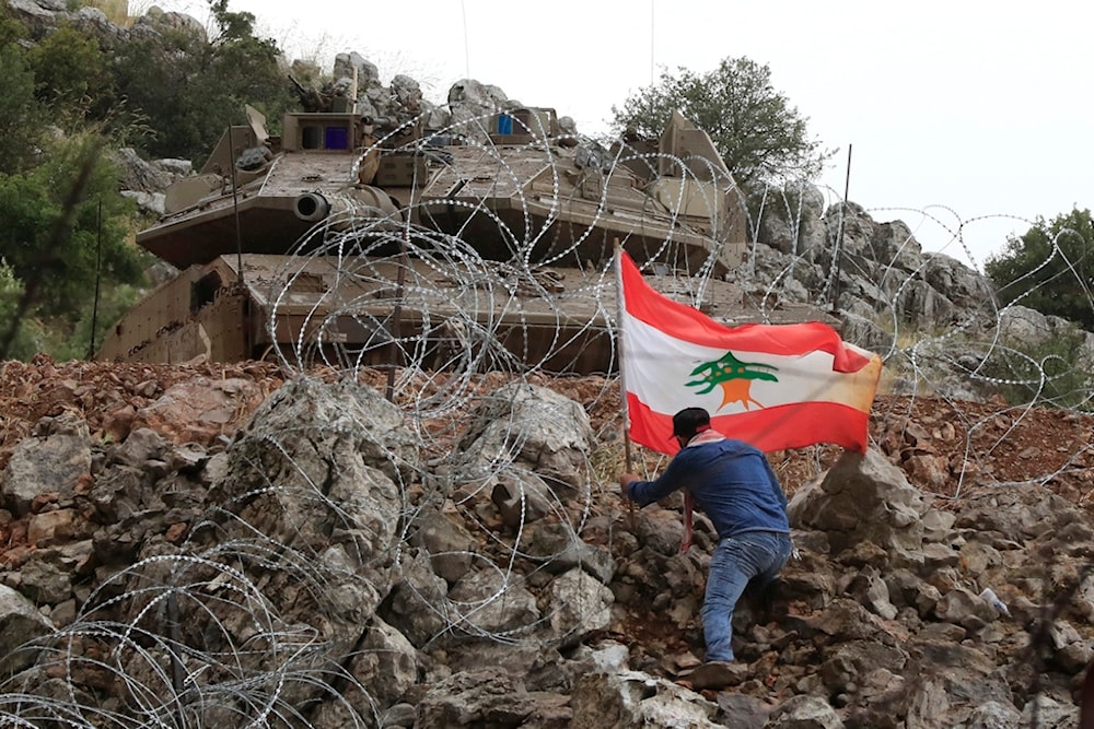 A Lebanese sets a Lebanese flag under a Israeli Merkava tank in the Kfar Shouba hills along the border, in south Lebanon, Friday, June 9, 2023 (AP)