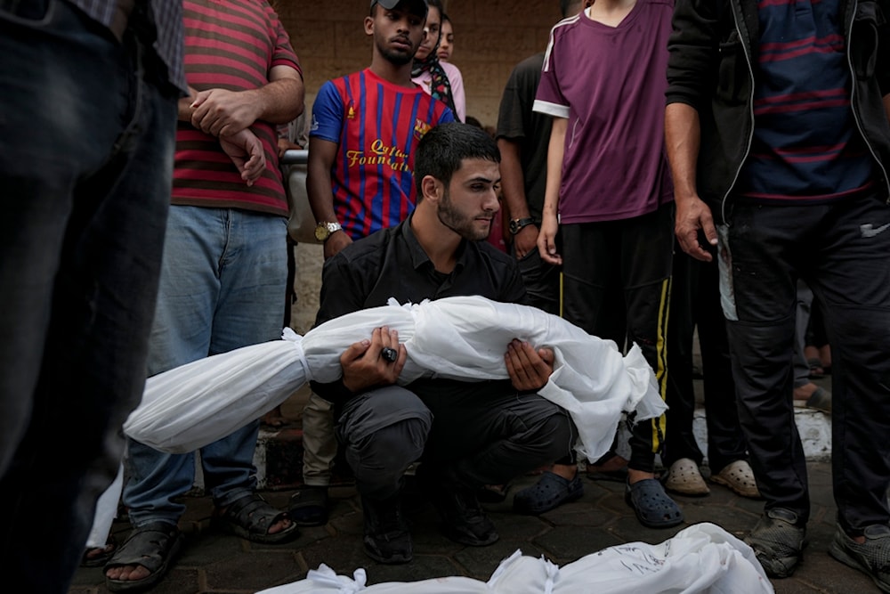 A Palestinian man holds the body of a relative killed in the Israeli bombardment of the Gaza Strip at a hospital morgue in Deir al-Balah, Tuesday, Oct. 8, 2024. (AP)