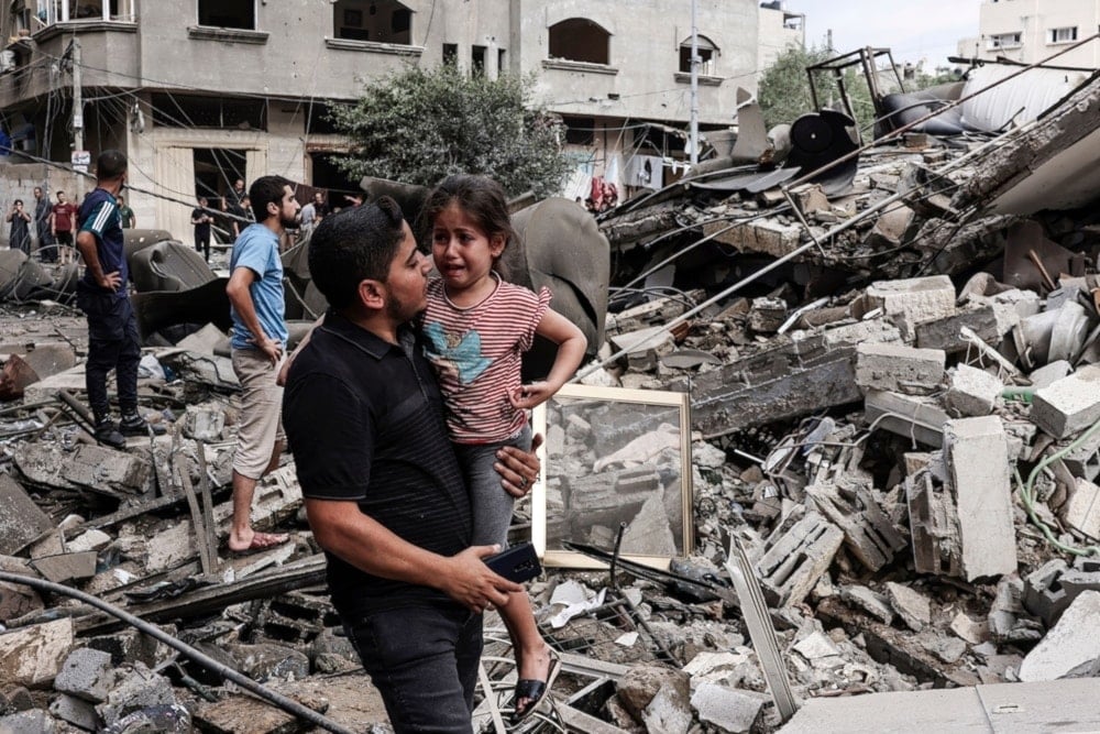 A Palestinian father carries his traumatized child as he walks in front of a residential building destroyed in an Israeli airstrike on Gaza City on October 7, 2023. (AFP)