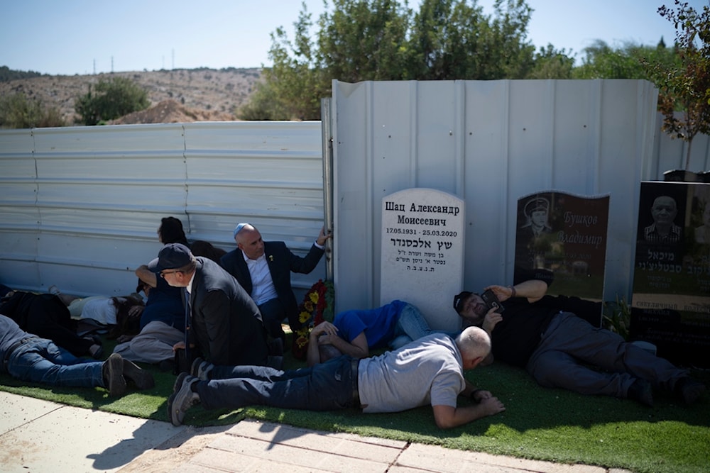 Settlers take cover as a siren warns of incoming rockets at the Tel Regev cemetery in the outskirts of Haifa, northern occupied Palestine, Monday, Oct. 21, 2024. (AP) 