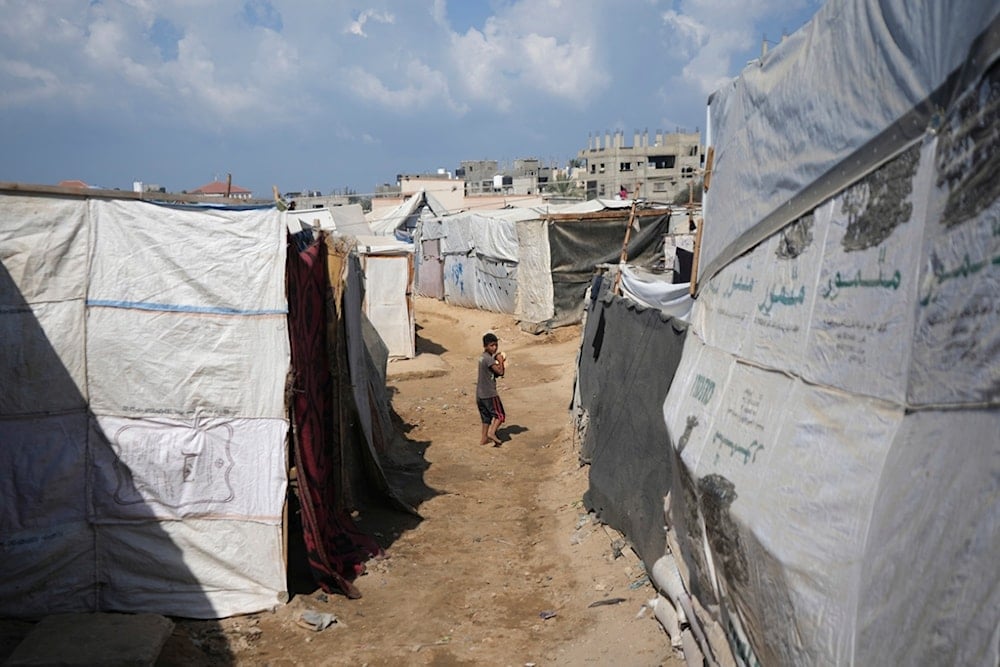 A displaced Palestinian boy carries bread as he walks between tents in Deir al-Balah, Gaza Strip, Friday, October 18, 2024 (AP)