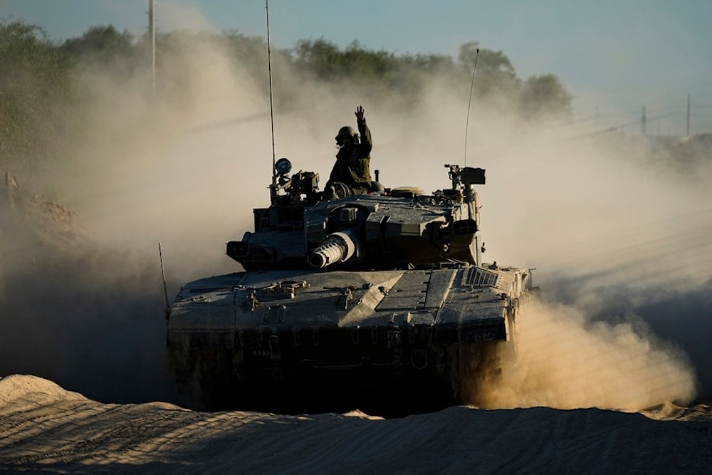 An Israeli soldier waves from a moving tank near the Gaza strip in southern occupied Palestine, Monday, Octpner 21, 2024 (AP)