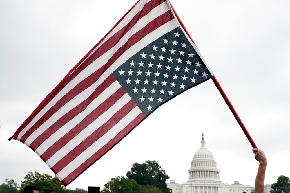 With the U.S. Capitol in the background, a demonstrator waves an upside down American flag before a rally in Washington, Saturday, Sept. 18, 2021. (AP)