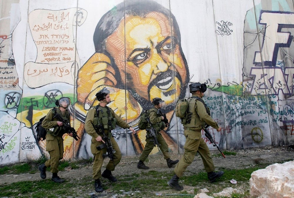 Israeli separation wall with portrait of leader Marwan Barghouti,with Israeli occupation soldiers patroling infront of it in the West Bank city of Ramallah, occupied Palestine, March 8, 2012. (AP)