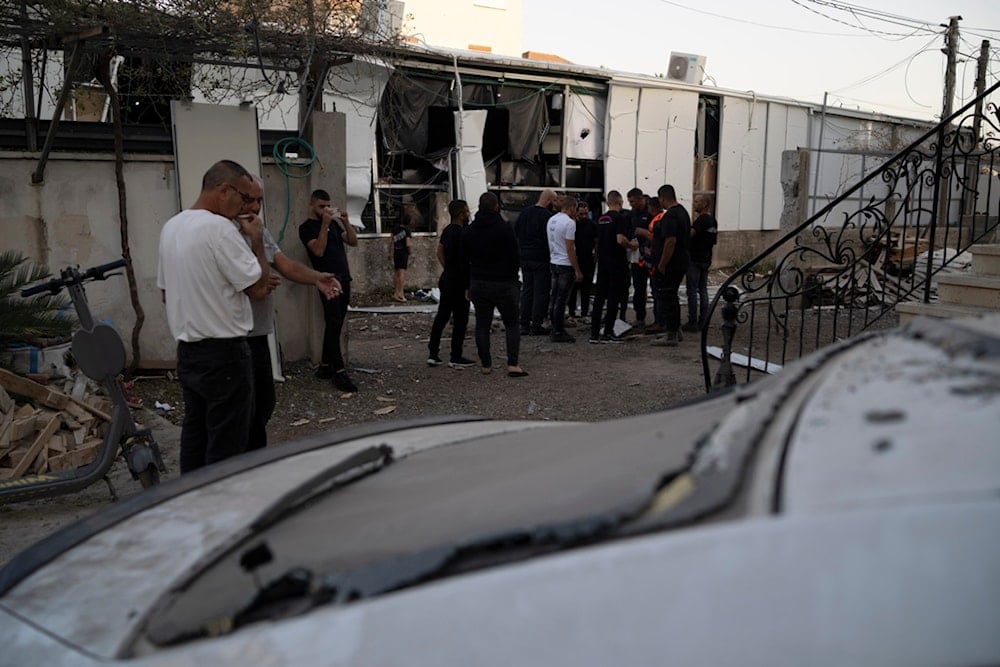 People stand next to an area of a local supermarket that was damaged by a rocket, fired from Lebanon, in Majd al-Krum, northern occupied Palestine, October 25, 2024 (AP)