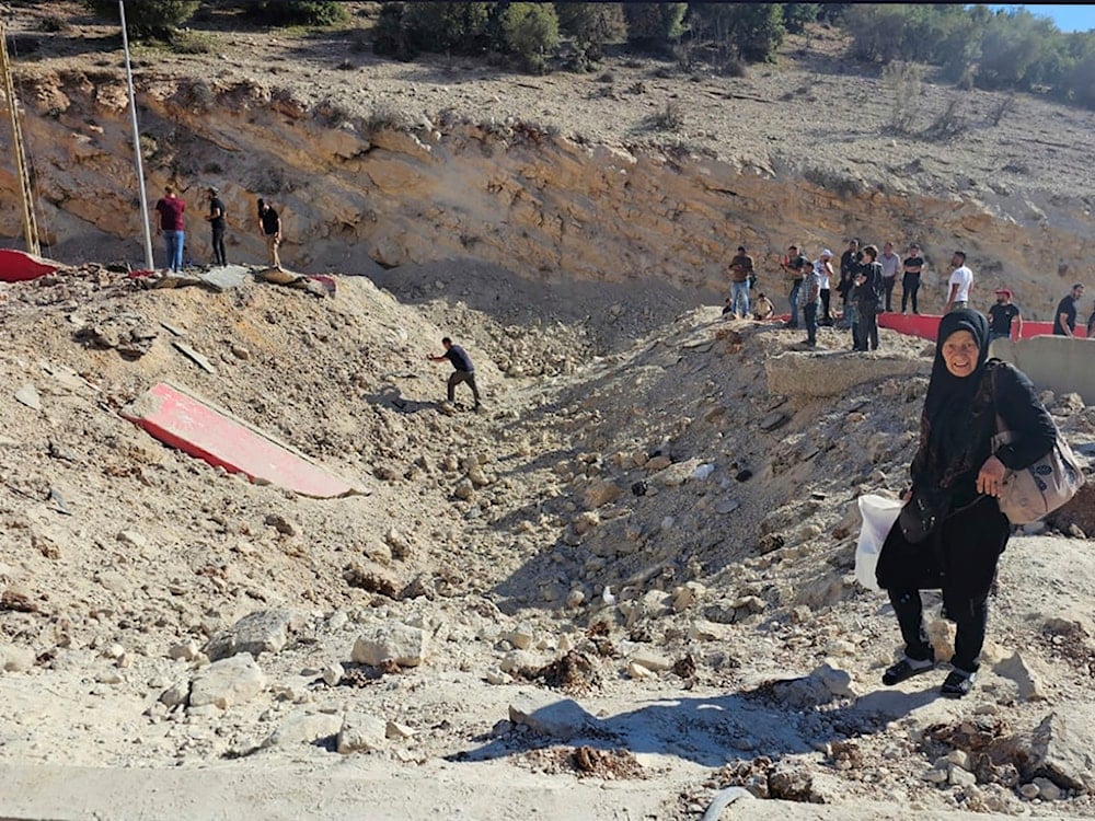 A woman carries her belongings crossing on foot into Syria through a crater caused by an Israeli airstrike to cut the road between the Lebanese and the Syrian checkpoints, Lebanon, Friday, Oct. 4, 2024. (AP)