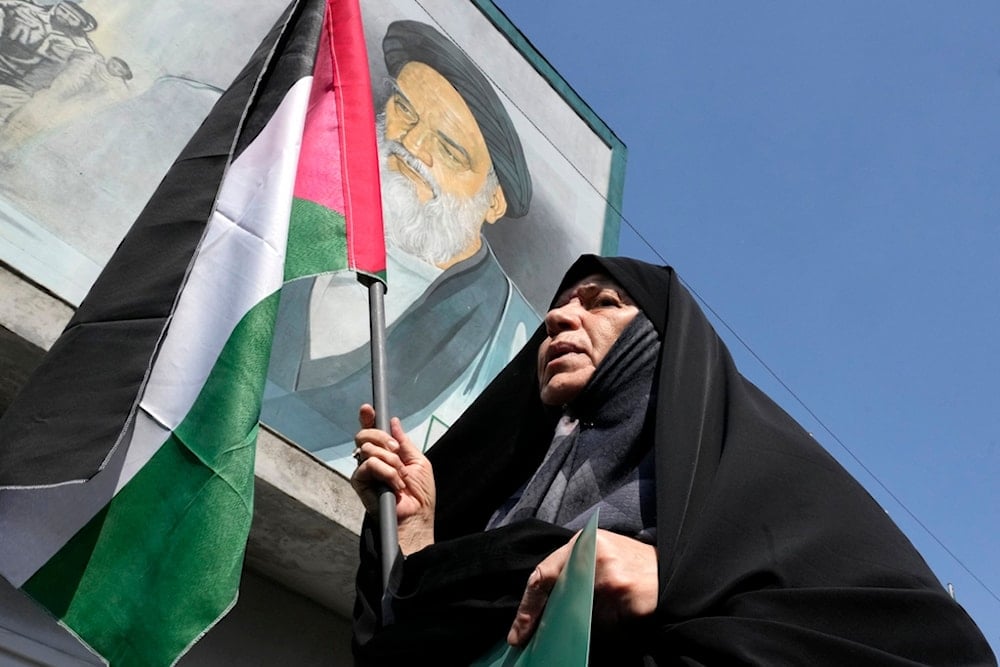 An Iranian woman holds a Palestinian flag in front of a mural of late revolutionary founder Ayatollah Khomeini, Iran, Friday, Sept. 27, 2024. (AP)