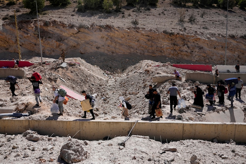 People carry their luggage as they cross into Syria on foot, through a crater caused by Israeli airstrikes aiming to block Beirut-Damascus highway at the Masnaa crossing, in the eastern Bekaa Valley, Lebanon, Saturday, Oct. 5, 2024. (AP)