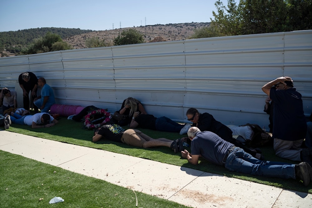 People take cover as a siren warns of incoming rockets fired from Lebanon, at the Tel Regev cemetery in the outskirts of Haifa, northern occupied Palestine, Monday, Oct. 21, 2024. (AP)