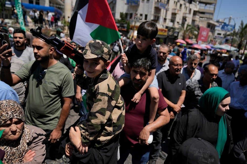 Palestinians carry children on their shoulders during a protest in the West Bank city of Ramallah, Wednesday, July 31, 2024 (AP)