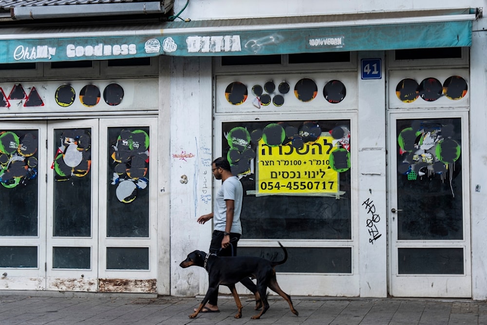 A settler walks his dog past a closed shop to rent in Tel Aviv, occupied Palestine, Thursday, Aug. 15, 2024. (AP Photo/Ariel Schalit)