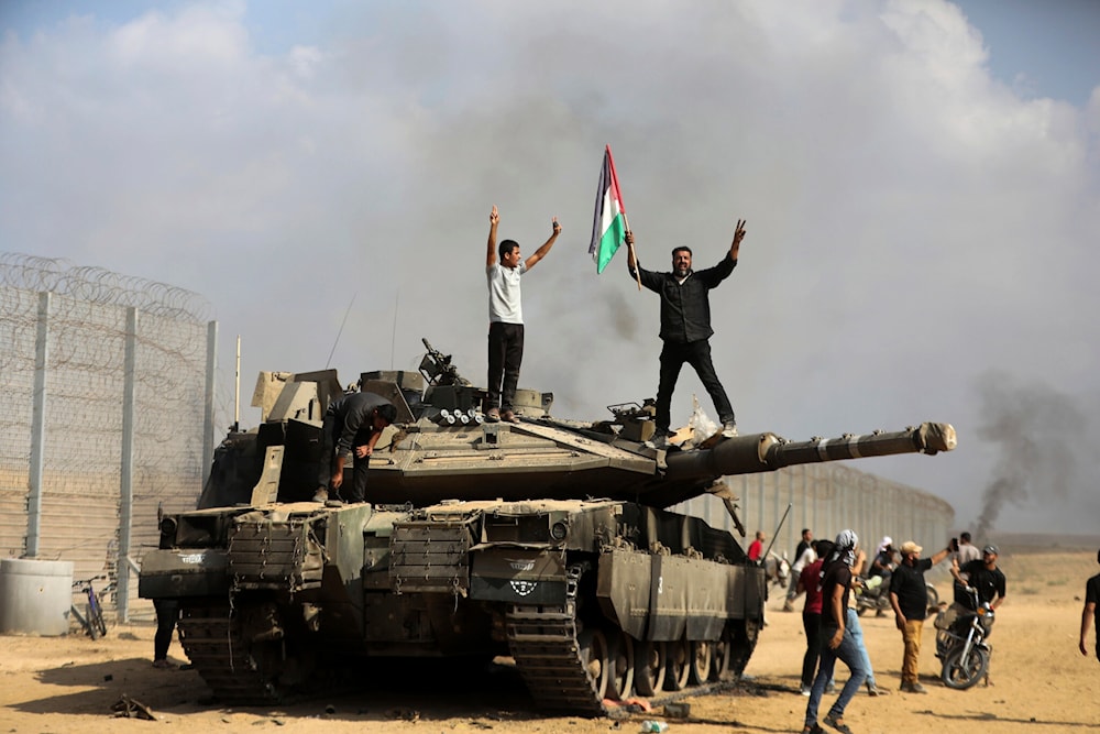 Gazans celebrate by a destroyed Israeli tank at the broken border fence, east of Khan Younis, October 7, 2023. (AP)