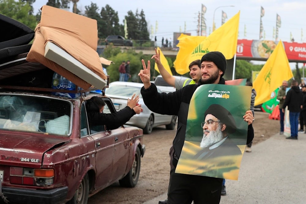 Men carry pictures of martyred Hezbollah leader Sayyed Hassan Nasrallah and the party's flag as displaced residents return to their villages after a ceasefire went into effect on Wednesday, November 27, 2024, in Ghazieh, Lebanon (AP)