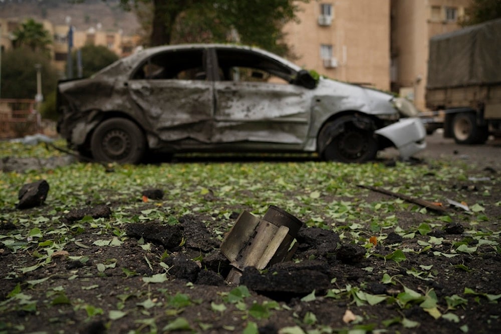 A rocket, fired from Lebanon during the night hours before the start of the ceasefire, sits wedged in the ground next to a damaged car in Kiryat Shmona, northern occupied Palestine, Wednesday, November 27, 2024 (AP)