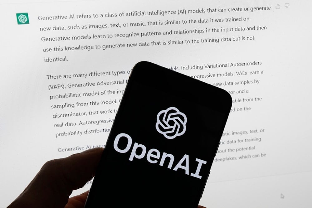 The OpenAI logo is seen on a mobile phone in front of a computer screen displaying output from ChatGPT, March 21, 2023 (AP)