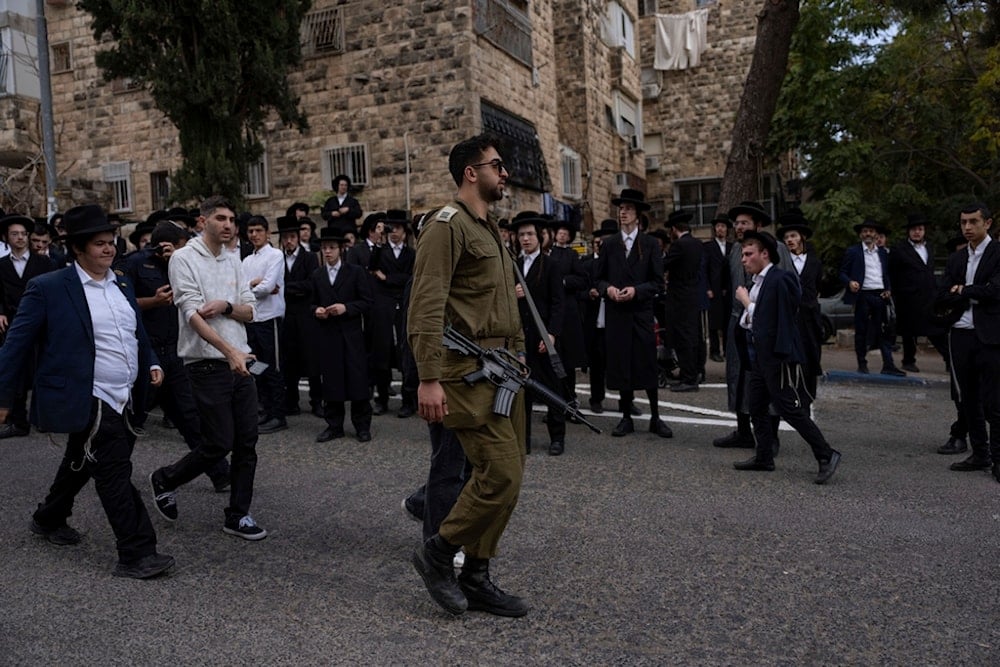 An IOF soldier walks among ultra-orthodox Jewish men during a protest against a potential new draft law which could end their exemptions from military service in al-Quds, Thursday, Oct. 31, 2024. (AP)