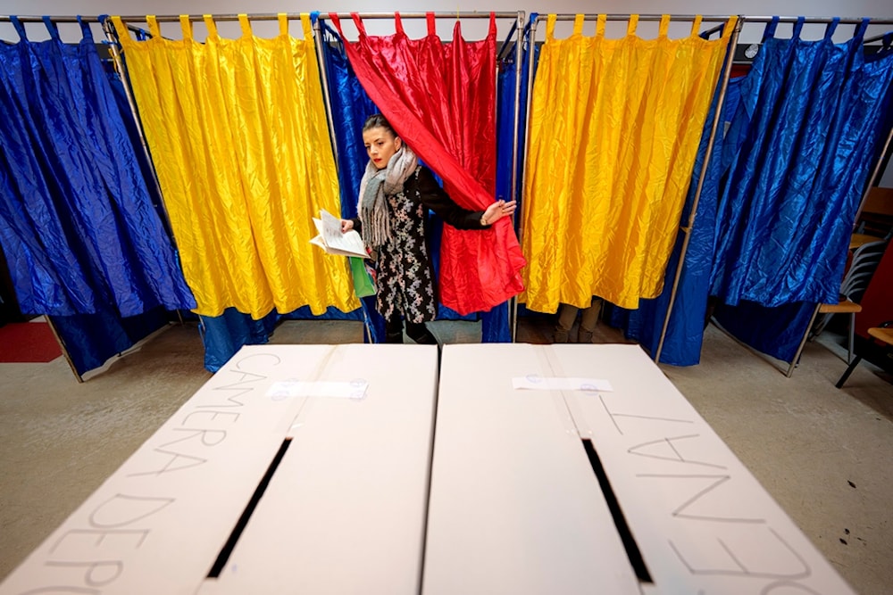 A woman exits a voting cabin with the colors of the Romanian flag as curtains before casting her vote in the country's parliamentary elections, in Bucharest, Romania, Sunday, December 1, 2024 (AP)