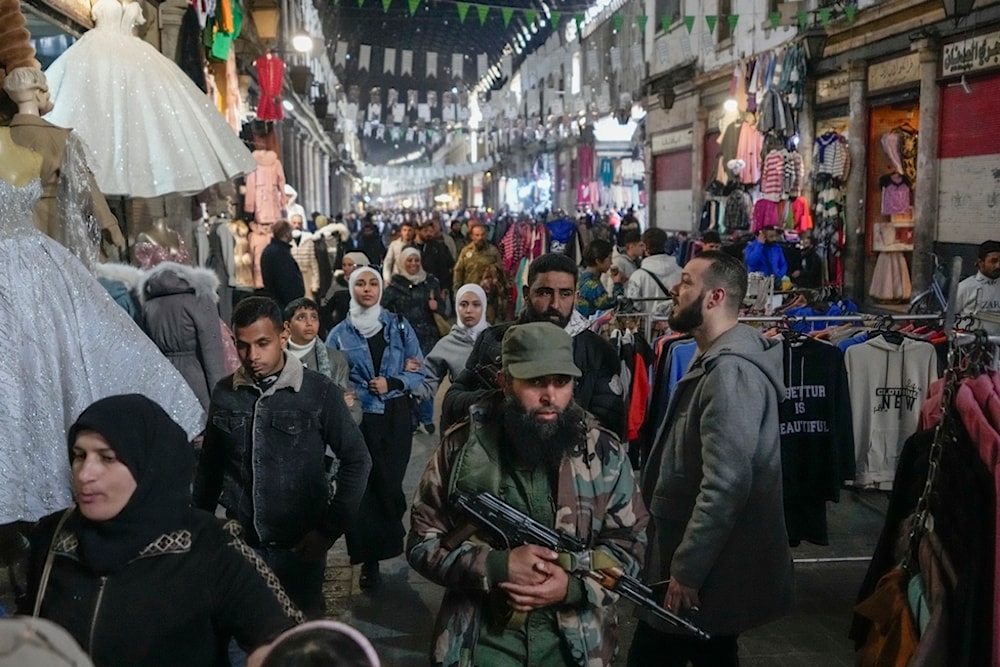 An armed opposition fighter walks among costumers at the al-Hamidiyeh market inside the old walled city of Damascus, Syria, Tuesday, December 10, 2024 (AP)