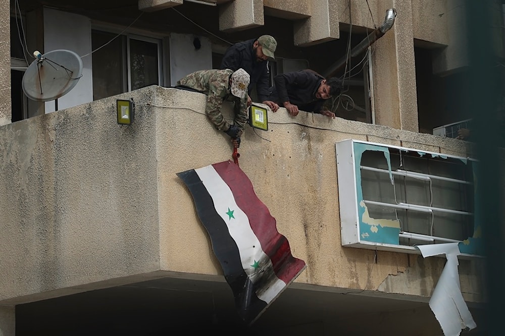 Syrian opposition fighters remove a government flag from an official building in Salamiyah, east of Hama, Syria, Saturday Dec. 7, 2024. (AP Photo/Ghaith Alsayed)