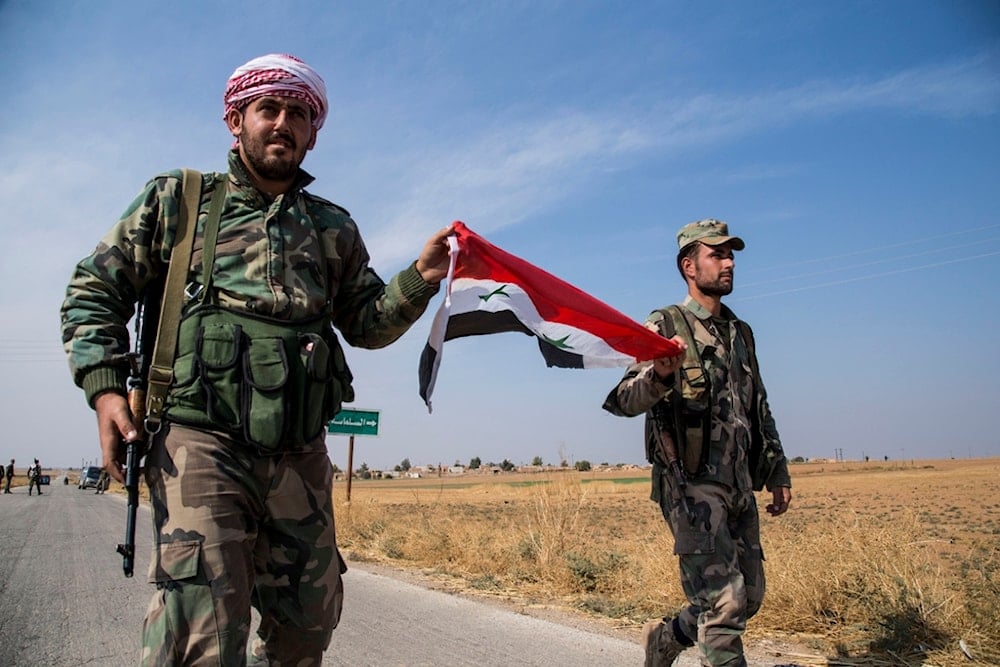 Syrian government forces carry a national flag as they walk at a checkpoint near the town of Tal Tamr, al-Hasakah, north Syria, on Oct. 22, 2019.  (AP)