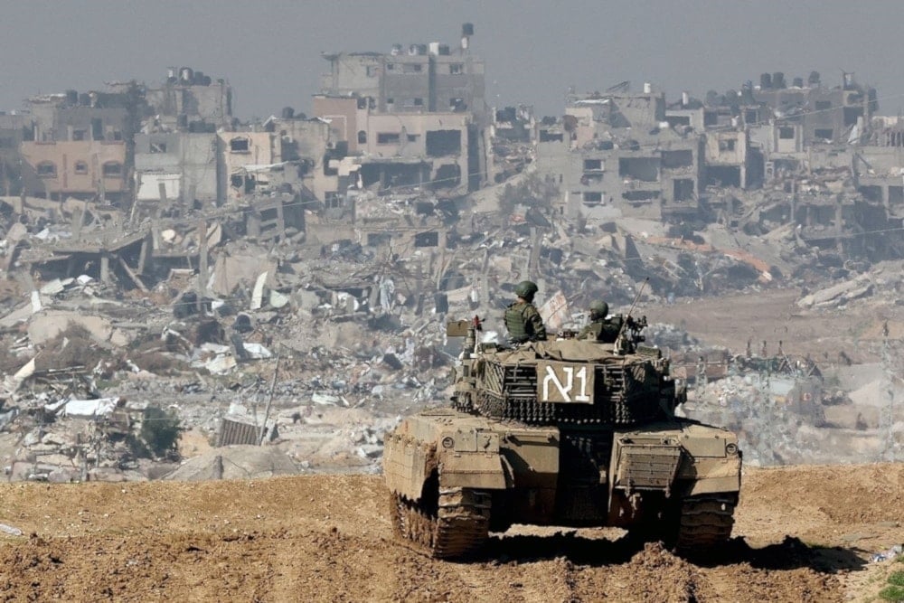 Israeli soldiers stationed atop a tank overlook residential areas in northern Gaza destroyed by Israeli bombardment in January 2024 (AFP)