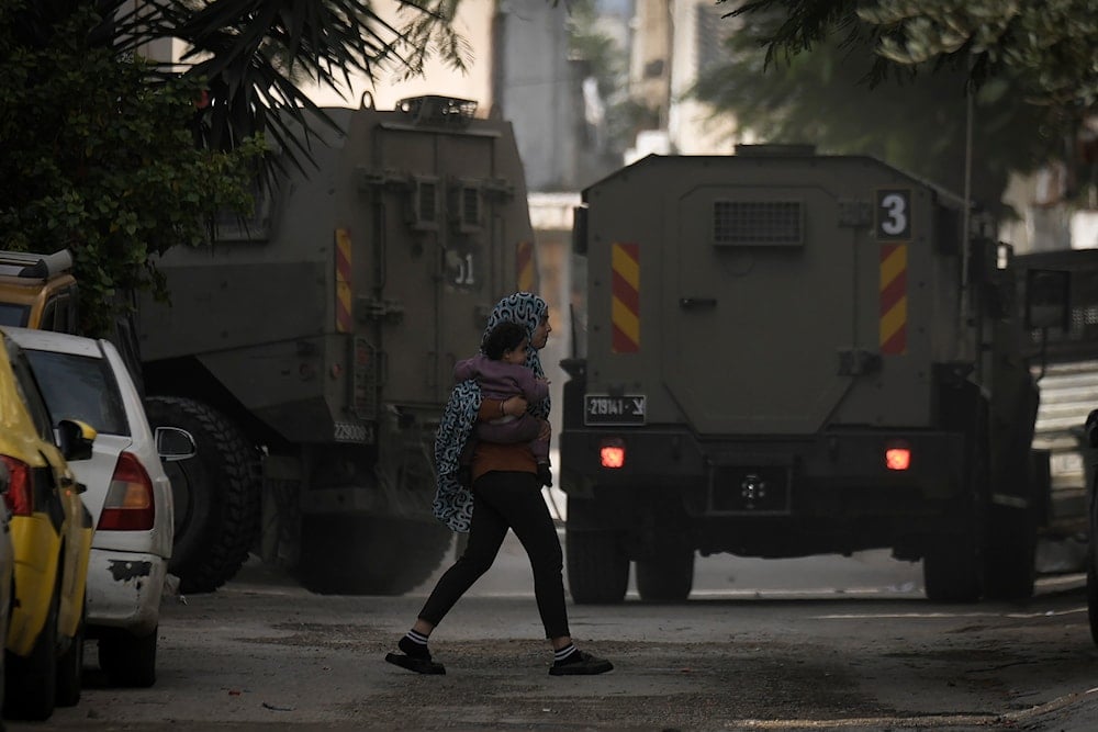 Palestinians walk next to an Israeli army vehicle during an army raid following a car that was hit by bullets in which a Palestinian was reportedly killed by Israeli special force, in the occupied West Bank city of Qalqilya, on December 12, 2024.(AP)