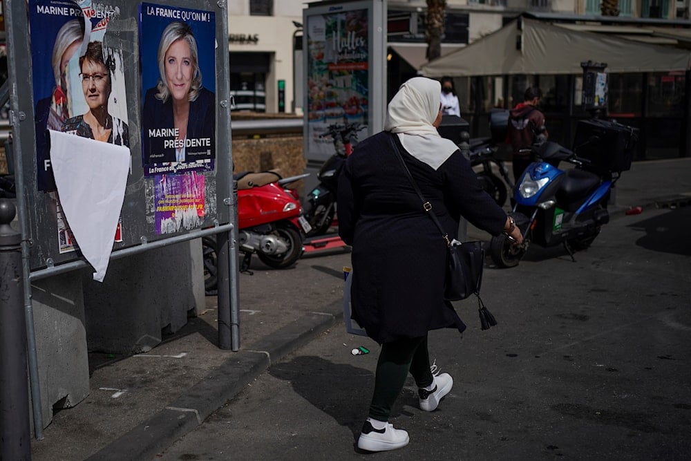 A woman walks by presidential campaign posters in Marseille, southern France, on April 13, 2022 (AP)