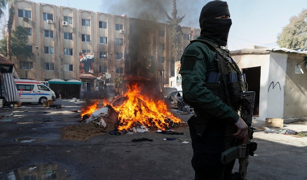 A Syrian militant stands next to fire as drugs and alcoholic beverages, found at a complex building, that are been destroyed in Damascus, Syria, Wednesday, Dec. 25, 2024. (AP)