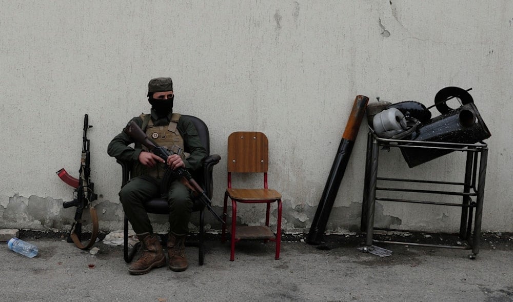 A member of the security forces of the newly formed Syrian government looks on as members of Bashar Assad's army line up to register as part of an 