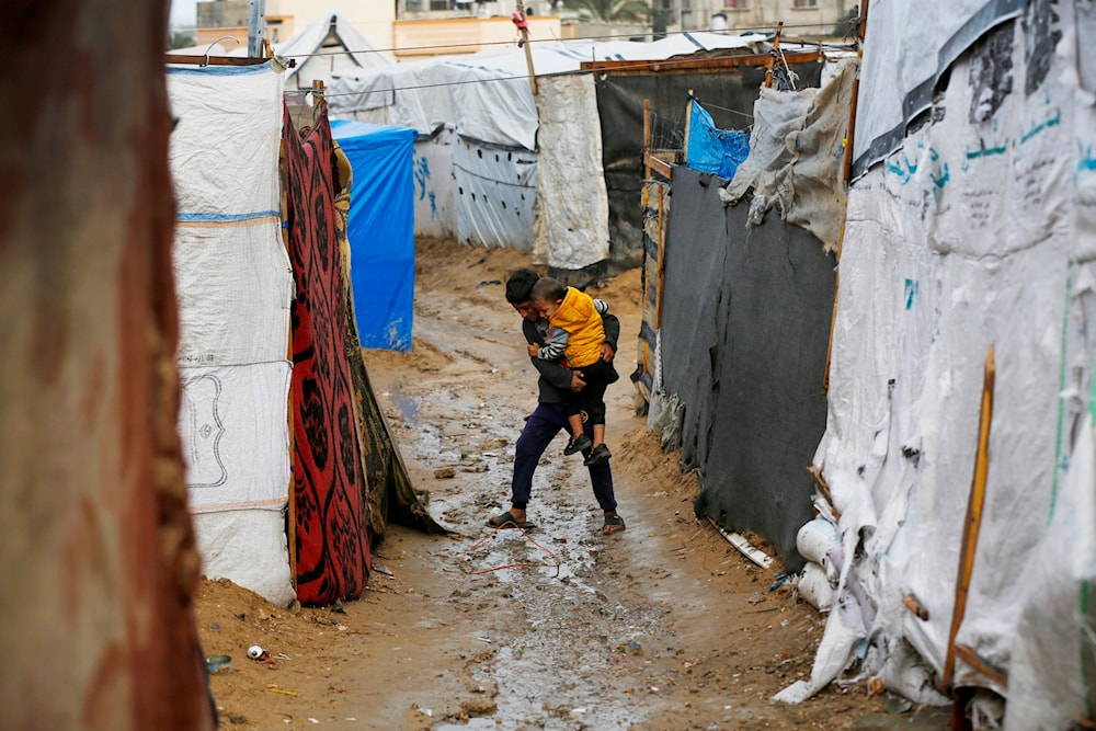 Two Palestinian children walking between tents as heavy rains cause flooding in the makeshift camps where thousands have taken shelter on November 28, 2024. (UNRWA)