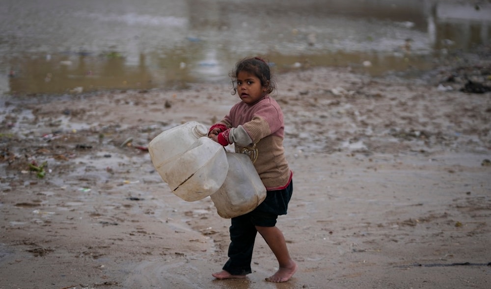 A young girl walks barefoot, carrying empty jerrycans to collect water, after overnight rainfall at the refugee tent camp for displaced Palestinians in Deir al-Balah, central Gaza Strip,, Tuesday, Dec. 31, 2024. (AP)