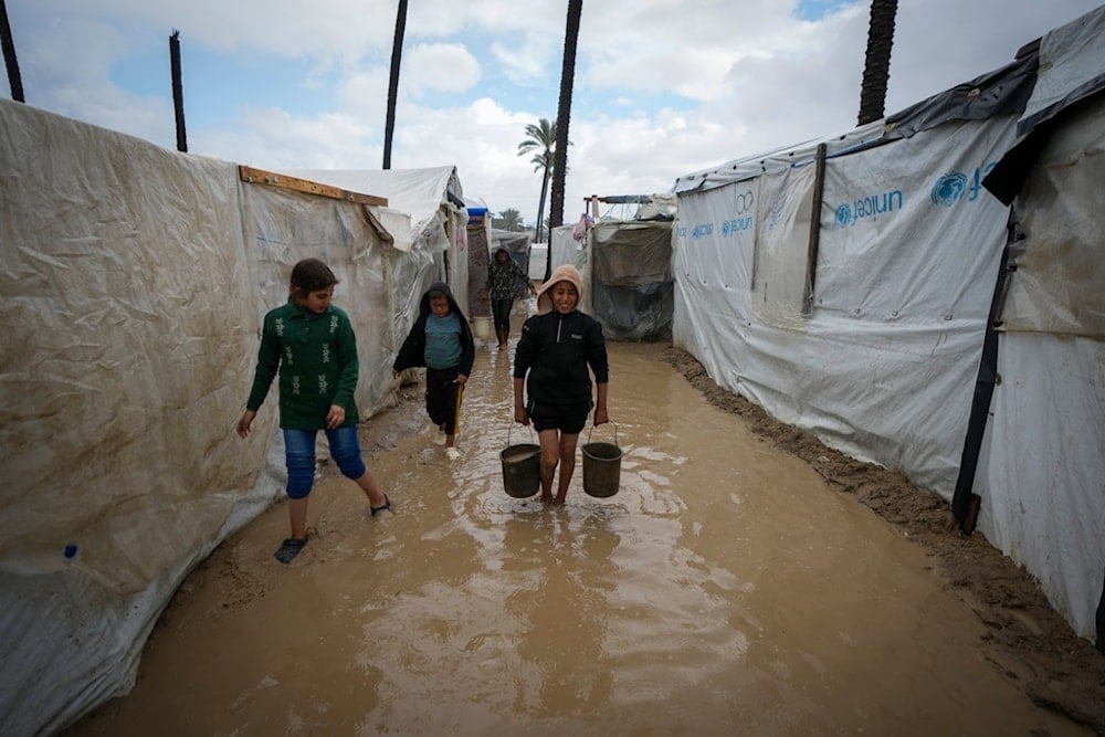 Palestinian children carry buckets of water after overnight rainfall at the refugee tent camp for displaced Palestinians in Deir al-Balah, central Gaza Strip, Tuesday, Dec. 31, 2024. (AP)