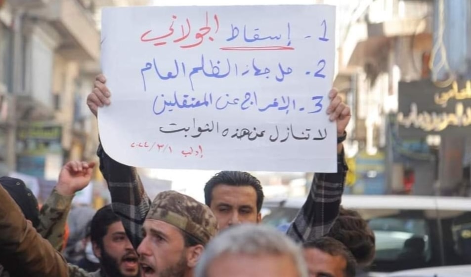 A photo showign a man carrying a sign urging the removal of al-Jolani in Idlib, Syria, during protests on March 1, 2024. (Social media)