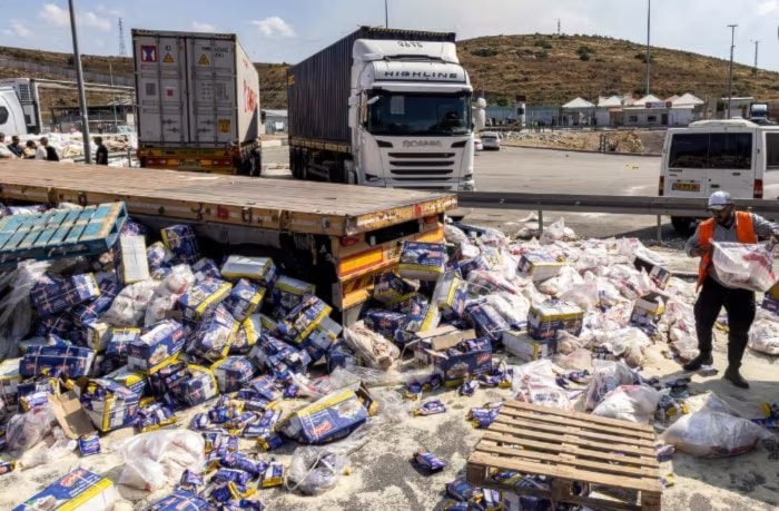 A worker clears piles of spilled food parcels scattered across the ground in a lorry park after Israeli settlers attacked Gaza aid trucks. (AFP/Getty Images)