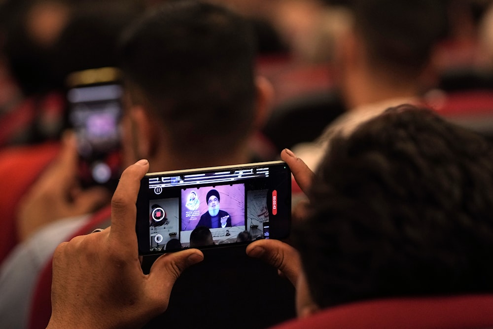 A man films a speech by Hezbollah leader Sayyed Hassan Nasrallah with a mobile phone as speaking via a video link, in the southern suburbs of Beirut, Lebanon, May 14, 2024 (AP)