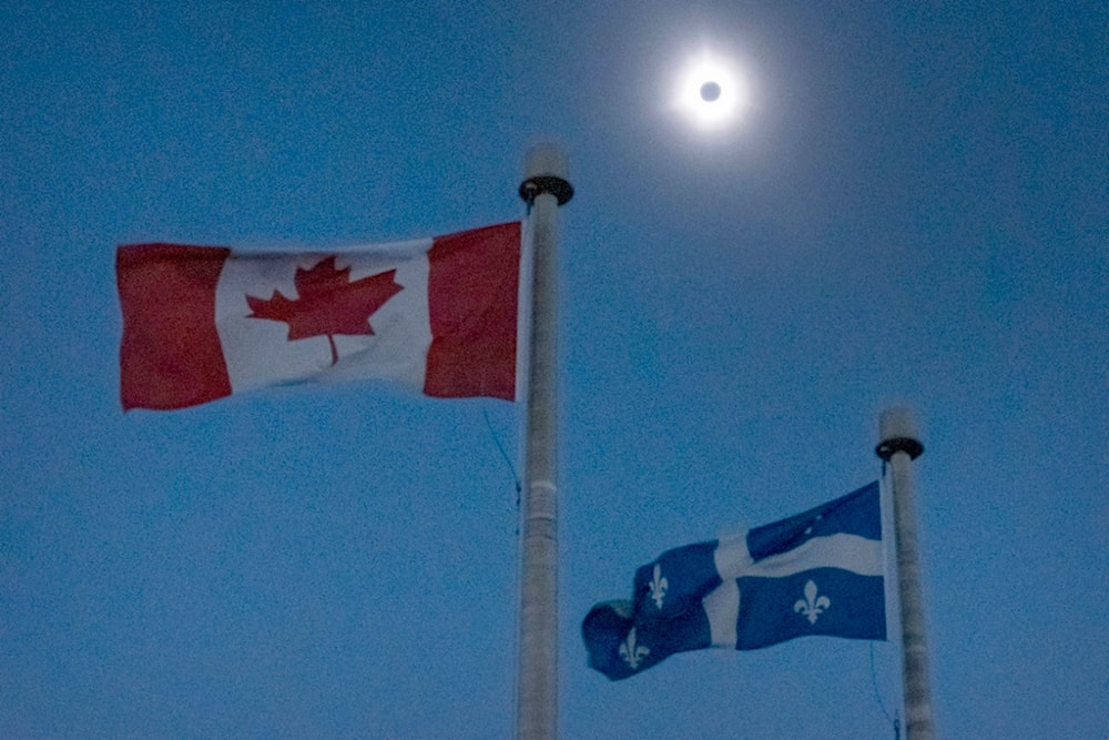 The moon covers the sun during a total solar eclipse, as Canadian and Quebec flags fly, as seen from Bishop's University in Sherbrooke, Quebec, Monday, April 8, 2024. (AP)