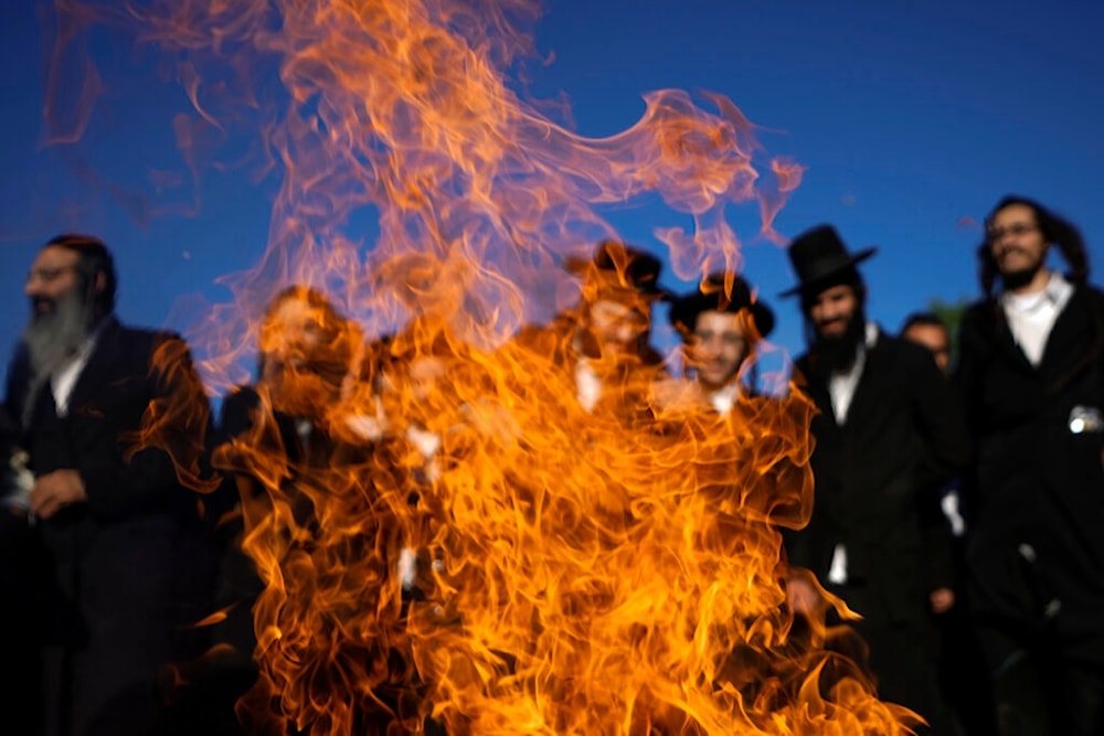 Ultra-Orthodox Jews dance around a bonfire during Lag B'Omer celebrations at the traditional grave site of Rabbi Shimon Bar Yochai at Jabal al-Jarmaq, occupied Palestine, Thursday, May 19, 2022 (AP)