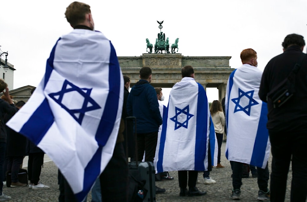 People, some draped with Israeli occupation flags attend a rally in solidarity with Israel near the Brandenburg Gate in Berlin, Germany, Wednesday, May 12, 2021. (AP)