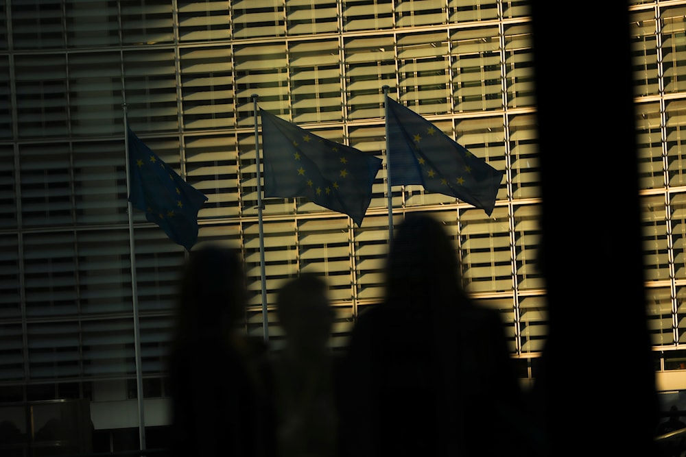 Members of the media look toward EU flags flapping in the wind outside EU headquarters during an EU summit in Brussels, on March 21, 2019. (AP)