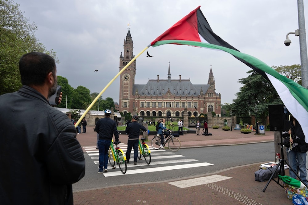 A lone demonstrator waves the Palestinian flag outside the Peace Palace, rear, housing the International Court of Justice, or World Court, in The Hague, Netherlands, Friday, May 24, 2024. 